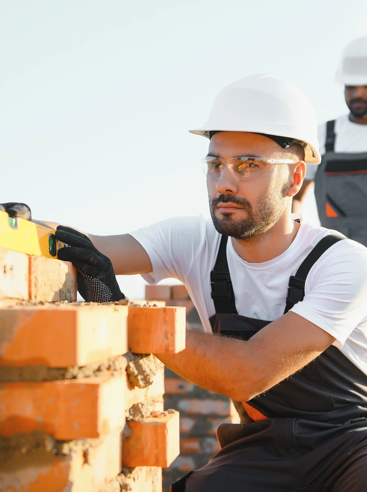 Two tradespeople laying bricks, one checking a wall with a spirit level. Illustrative photograph.